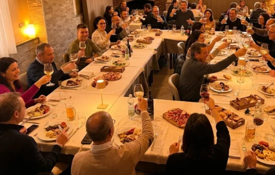 Cena conviviale all'Osteria I 2 Baséj Una sala del ristorante piena di commensali che cenano e brindano, in un'atmosfera calda e accogliente con luci soffuse.